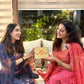 Two women in traditional attire exchanging a colorful gift box.