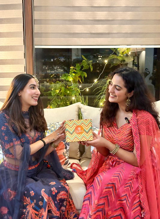 Two women in traditional attire exchanging a colorful gift box.